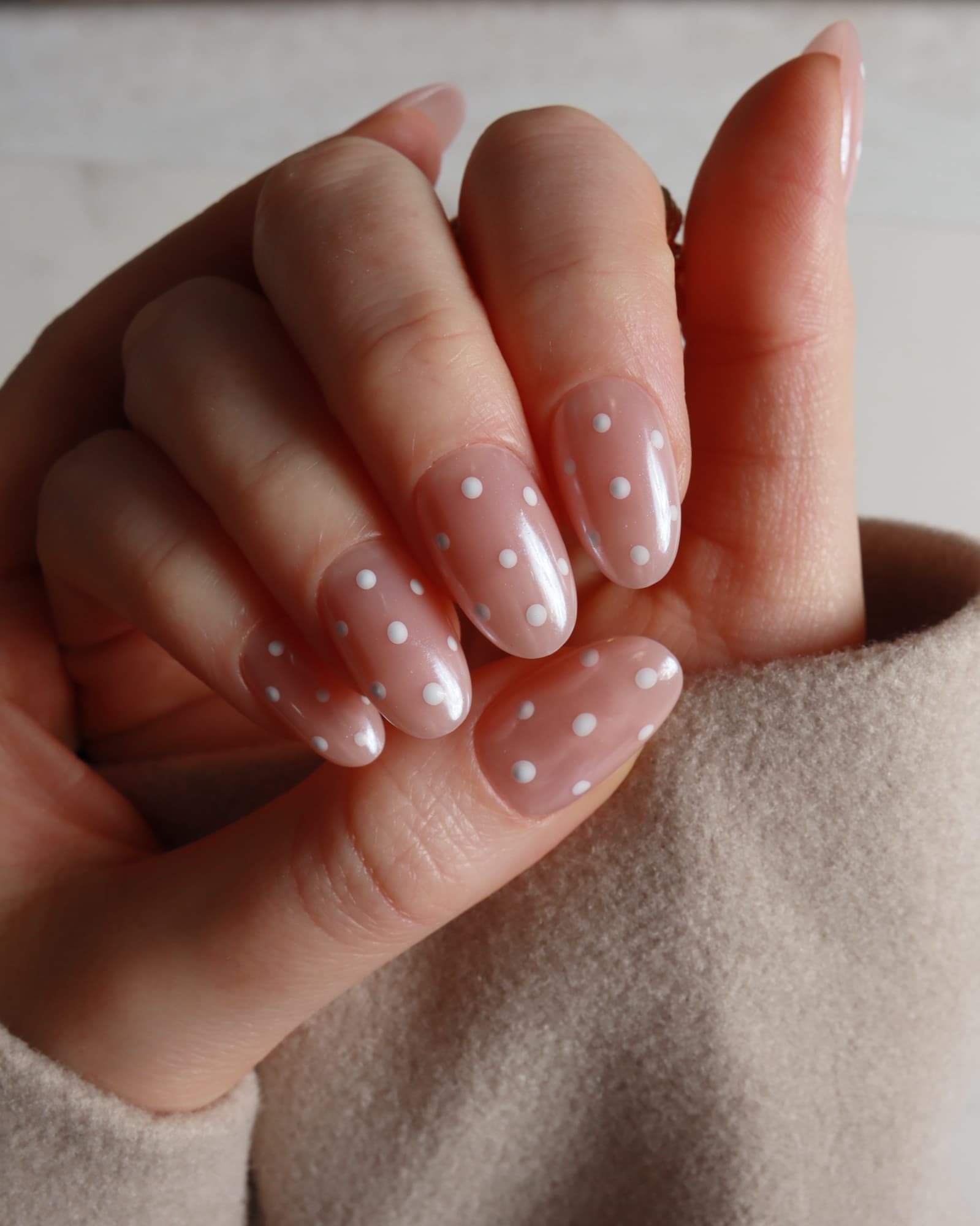 Hand with pink nail polish featuring white polka dots on a neutral background