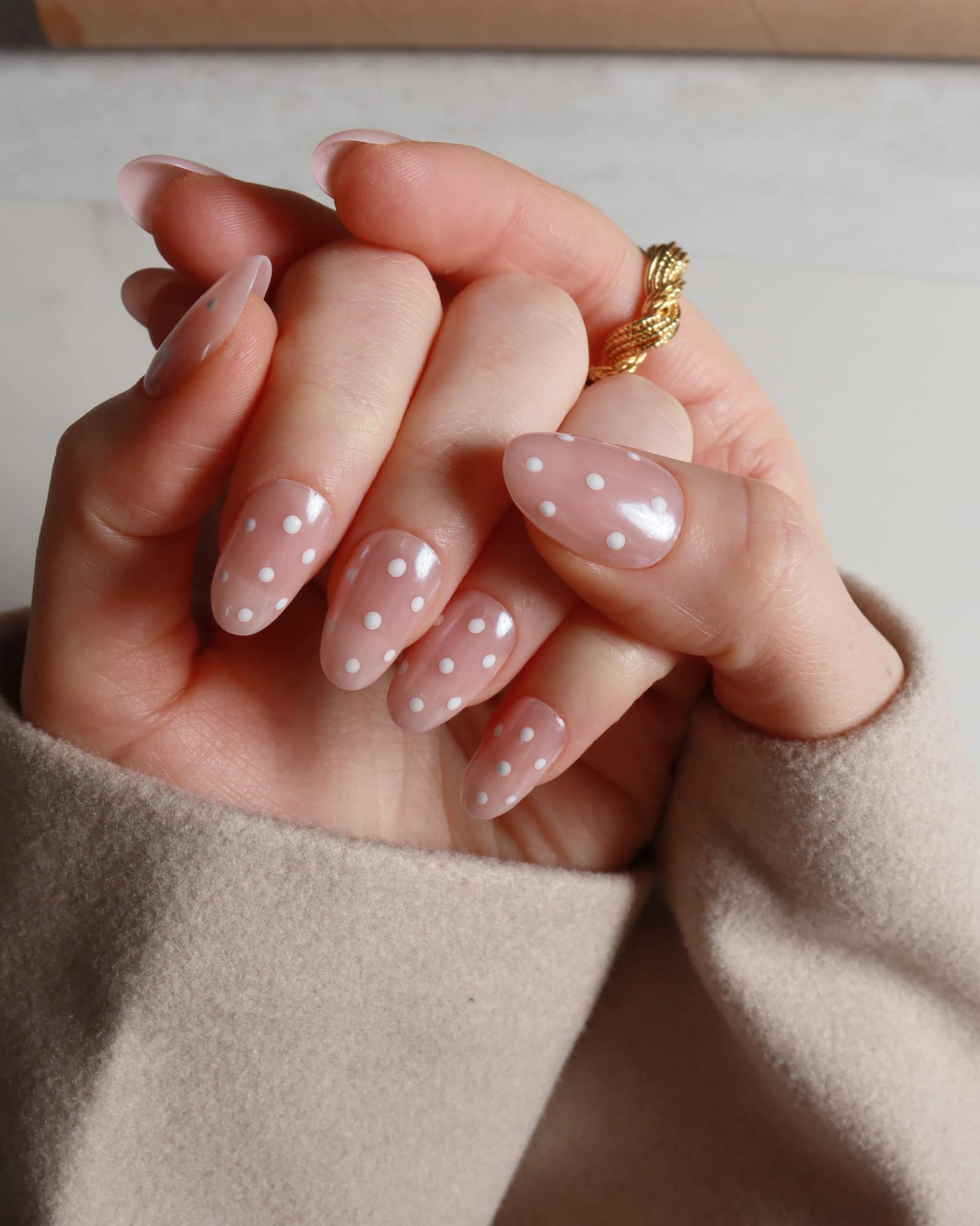 Hand with polka dot nail design wearing a gold ring on a neutral background